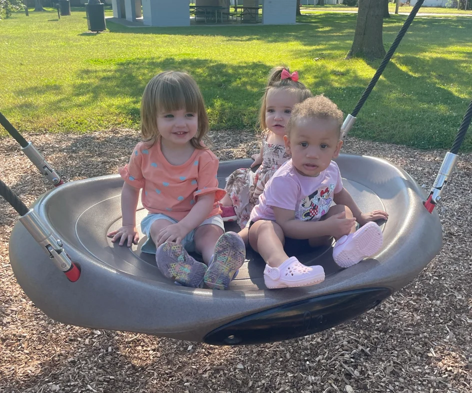 Three toddlers enjoying a saucer swing together outdoors on a sunny day