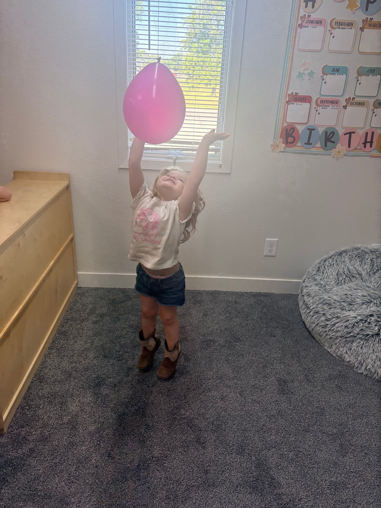 Toddler girl stretching both arms overhead to bat a pink balloon during indoor movement play