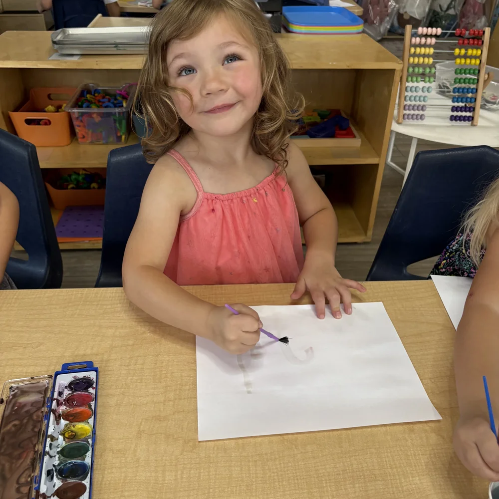 Preschool girl smiling while painting with watercolors during art time at The Nest