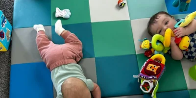 Two infants playing on a soft padded mat with toys in the Owlets infant room at The Nest in Earlham, Iowa