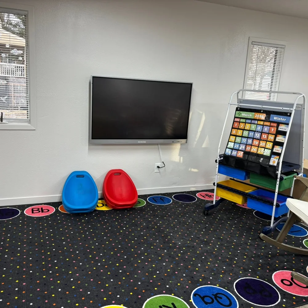 Preschool circle time area with alphabet carpet, calendar easel, and interactive display screen