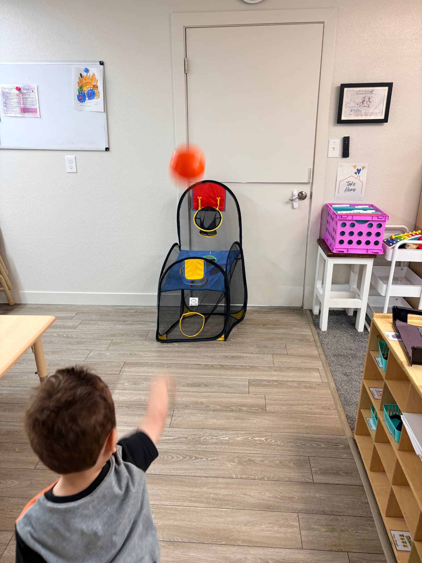 Toddler boy watching the orange ball fly toward the indoor basketball hoop during active indoor play