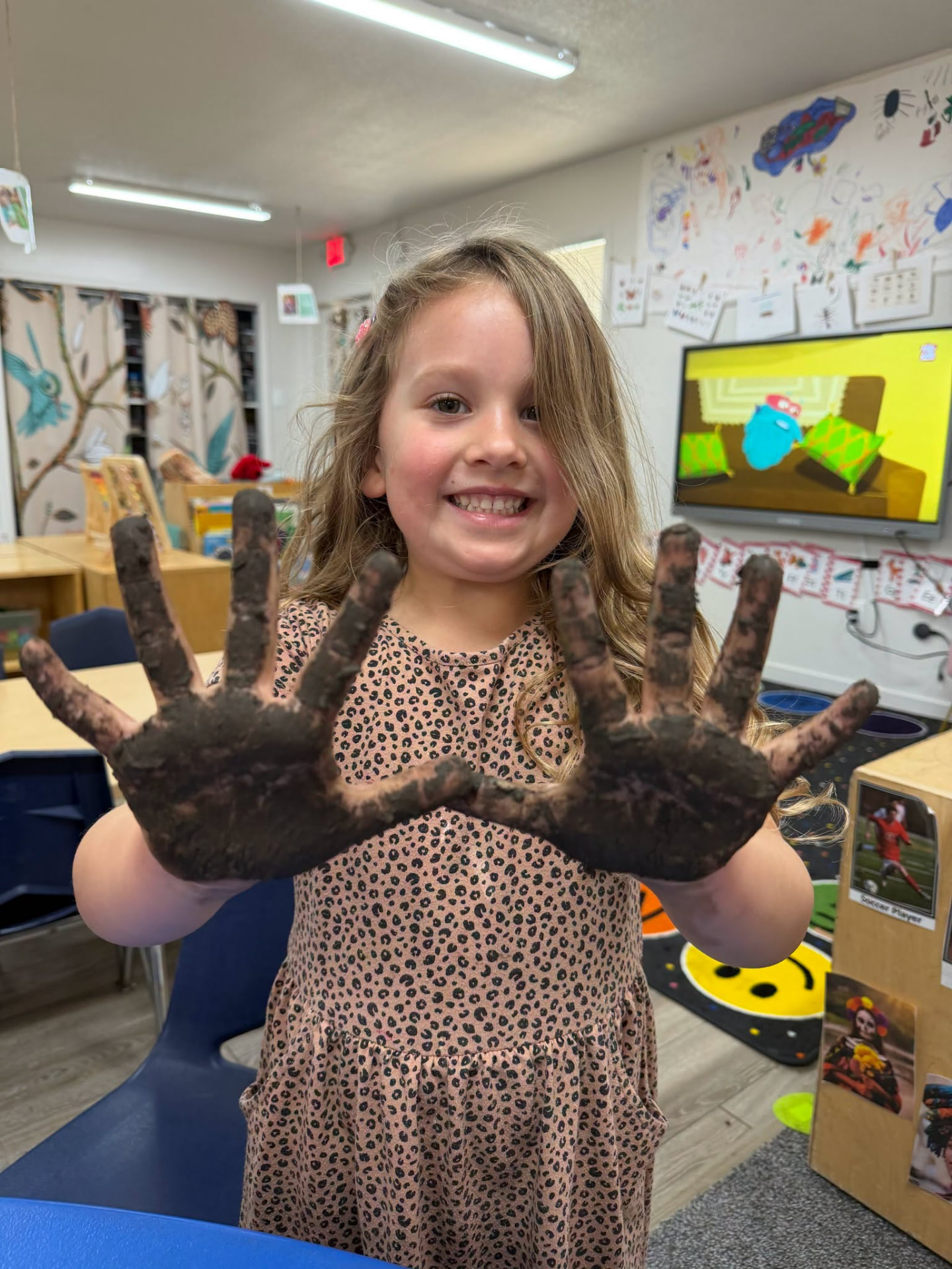 Smiling school age girl showing muddy hands after outdoor summer play at The Nest