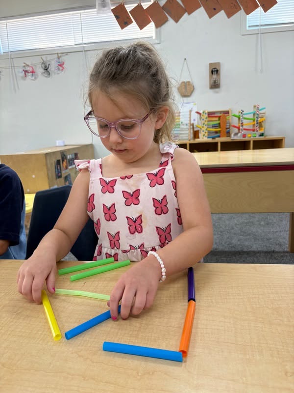 School age girl in glasses arranging straws into geometric shapes at The Nest
