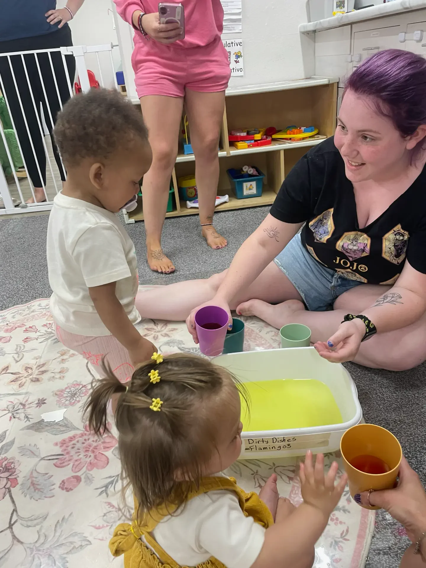 A teacher and toddlers doing a colorful water pouring activity in the Flamingos transition room