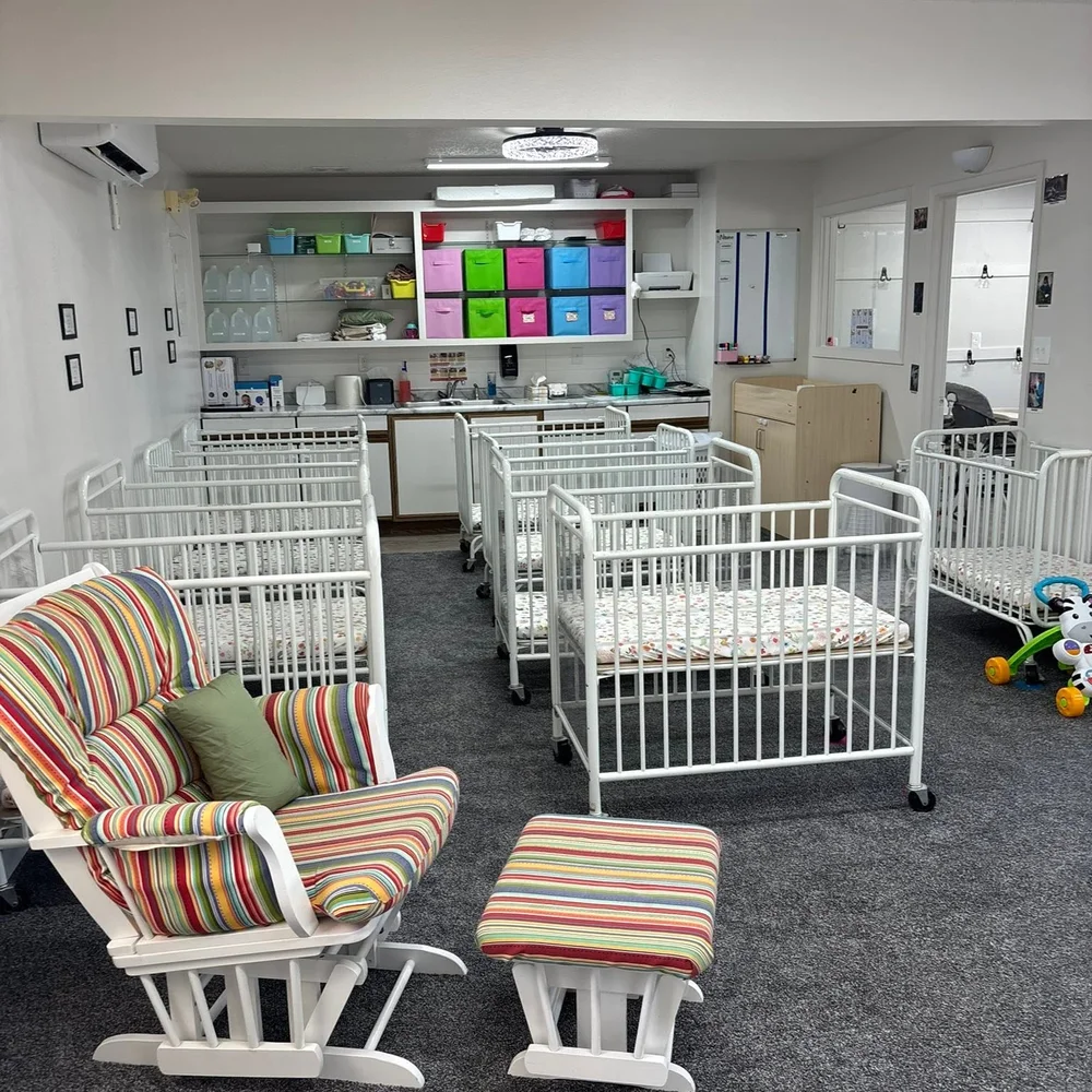 The Owlets nursery at The Nest in Earlham, Iowa with rows of white cribs, a striped glider rocker, and a diapering and bottle prep station