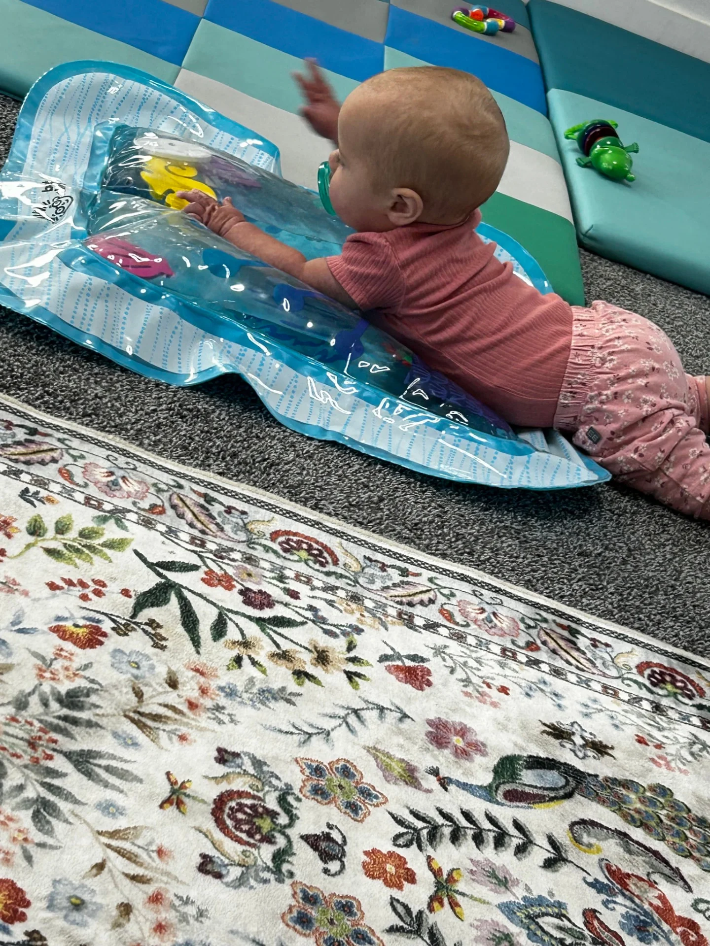 Infant in pink doing tummy time on a blue sensory water play mat with floating shapes at The Nest