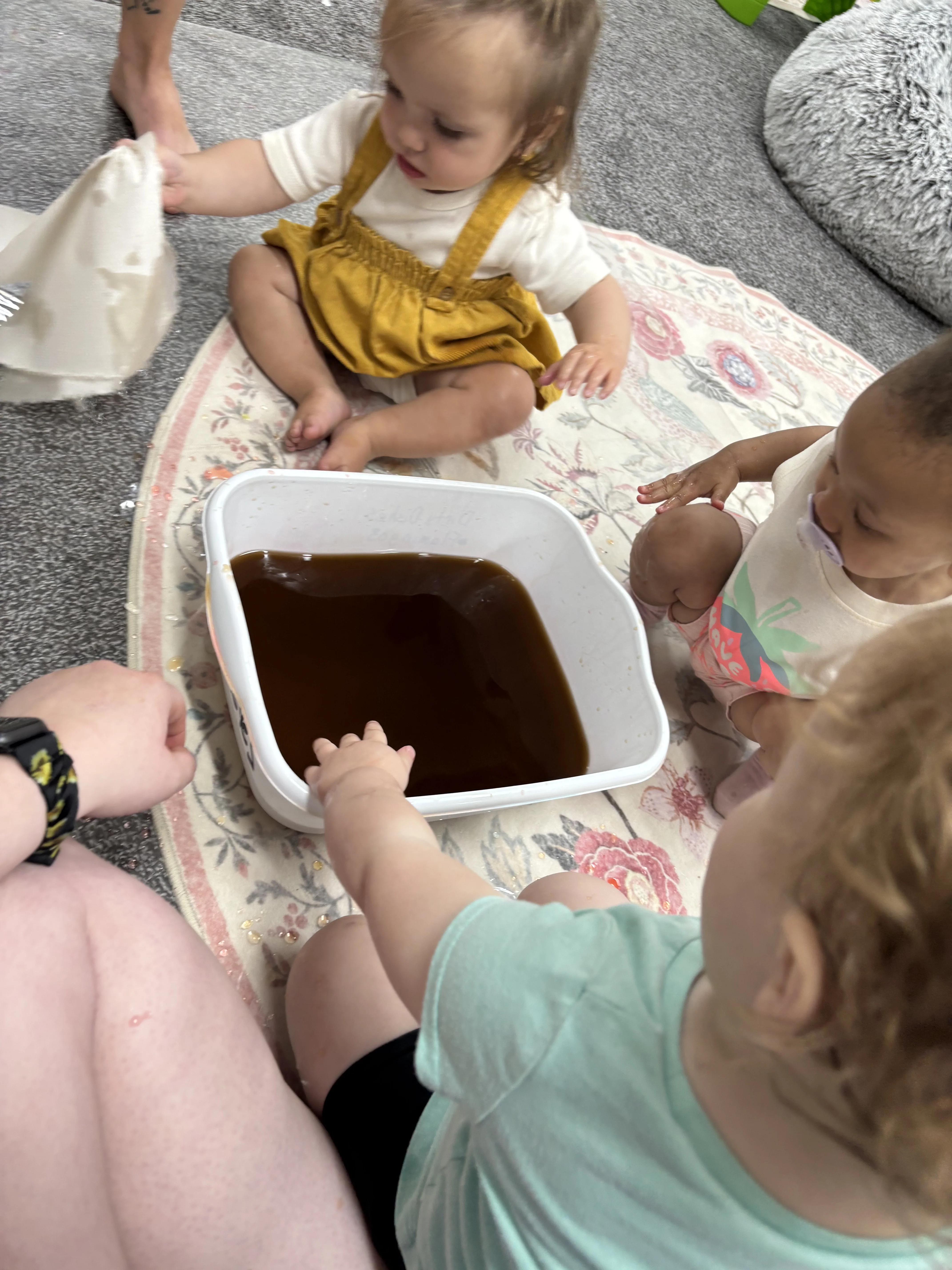 Toddler touching a mirror while exploring her reflection with a caregiver nearby