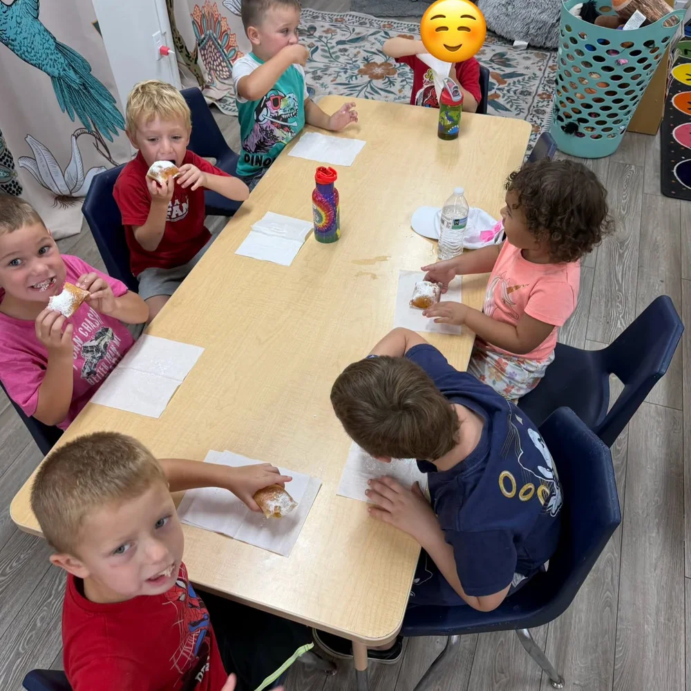 Preschoolers sitting around a long table eating pastries and drinking water during snack time at The Nest