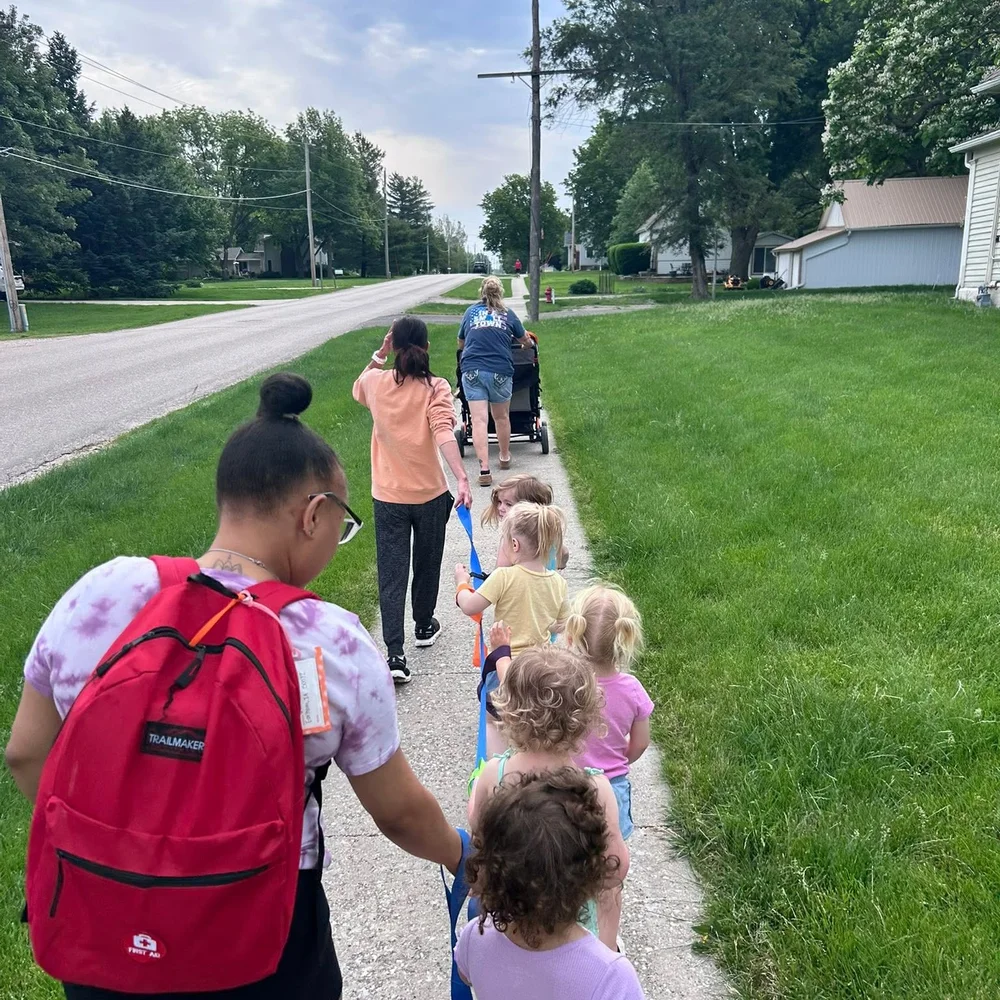 Teachers and toddlers holding a walking rope on a neighborhood stroll through Earlham, Iowa