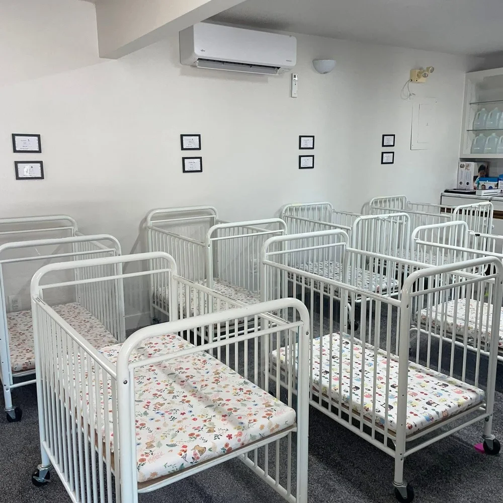 Individual white cribs with floral and animal print sheets in the infant sleep area at The Nest