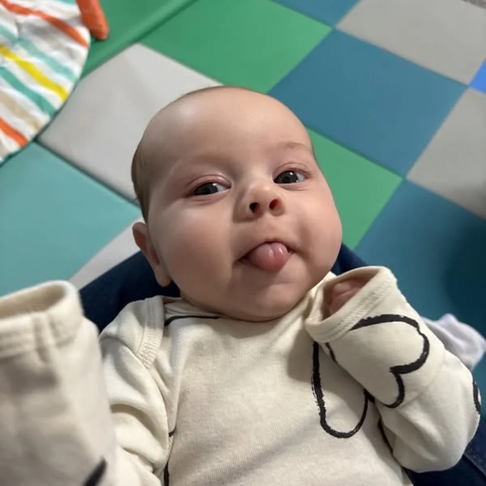 Happy infant lying on a checkered foam play mat sticking out their tongue